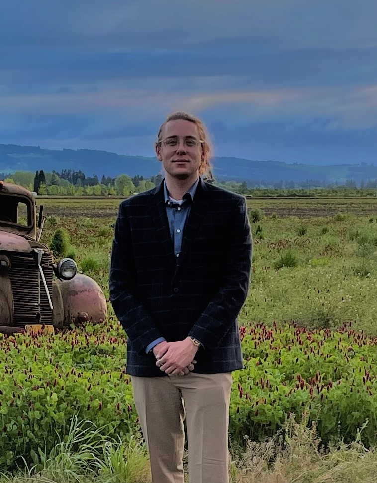 Portrait of Quinn N. Liebbe in a field with a vintage truck and mountain backdrop